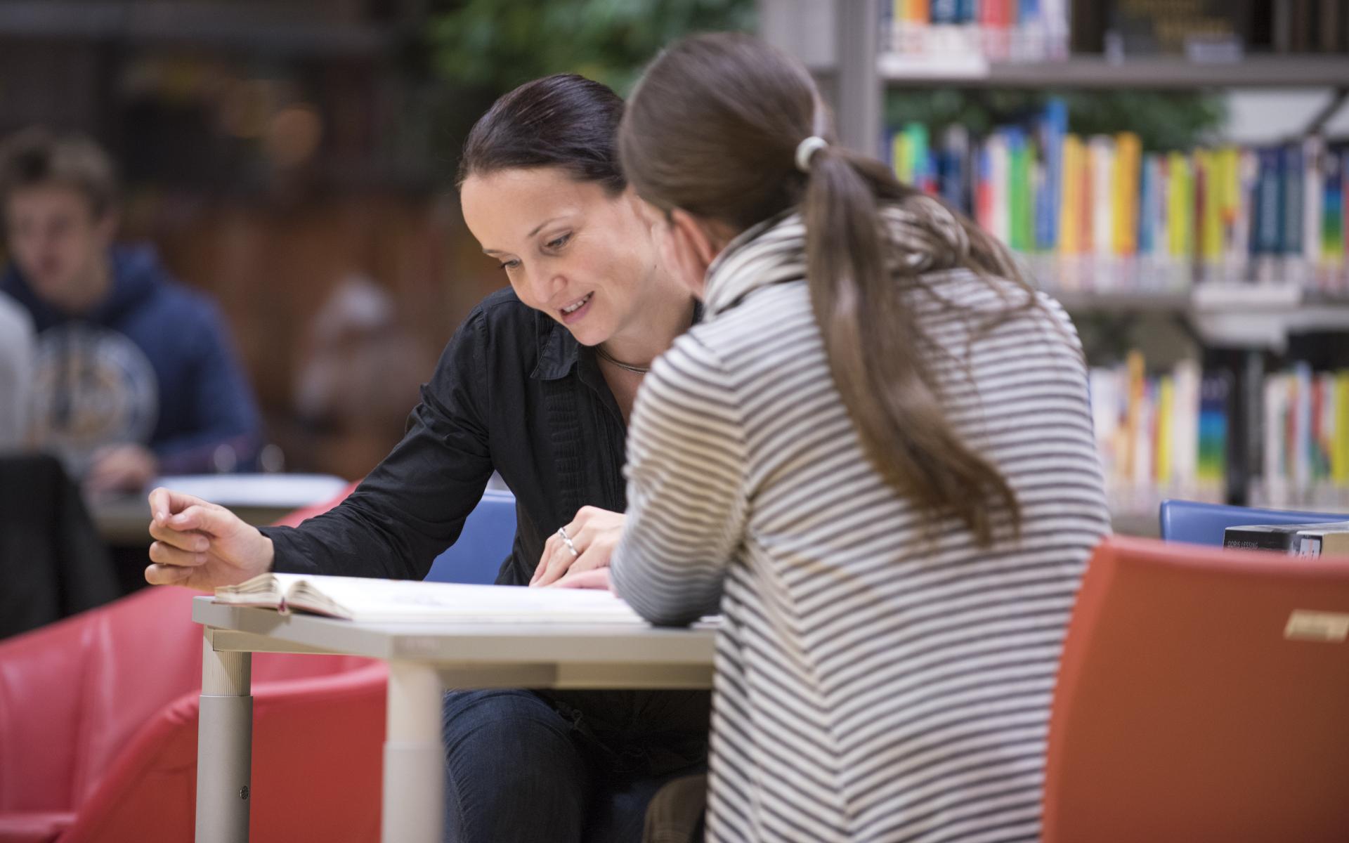 Zwei Frauen sitzen an einem Tisch und betrachten ein Buch